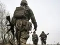 Żołnierze w ukraińskich mundurach, z karabinami, idą przez zarośla. Czy mężczyźni mogą wyjechać z Ukrainy?