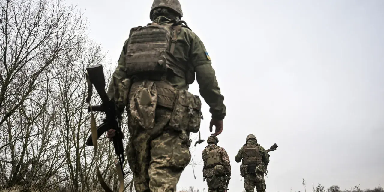 Żołnierze w ukraińskich mundurach, z karabinami, idą przez zarośla. Czy mężczyźni mogą wyjechać z Ukrainy?