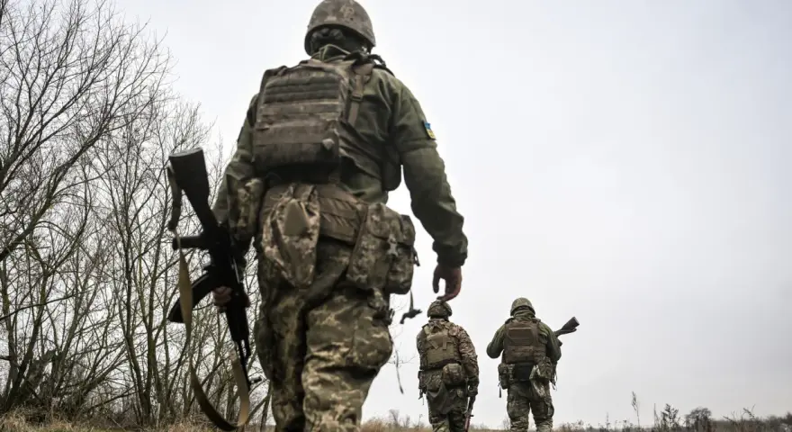 Żołnierze w ukraińskich mundurach, z karabinami, idą przez zarośla. Czy mężczyźni mogą wyjechać z Ukrainy?