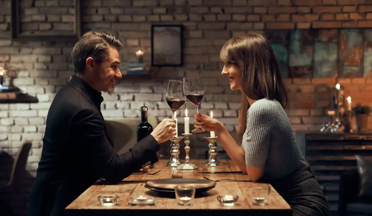 Para randkę w domu, postaw na elegancką, ale wygodną stylizację. On w czarnym garniturze, ona w szarym sweterku i spódnicy.